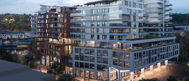 Moderne leilighetskompleks med glassfasader og næringsarealer på gateplan, kveldsbelysning.